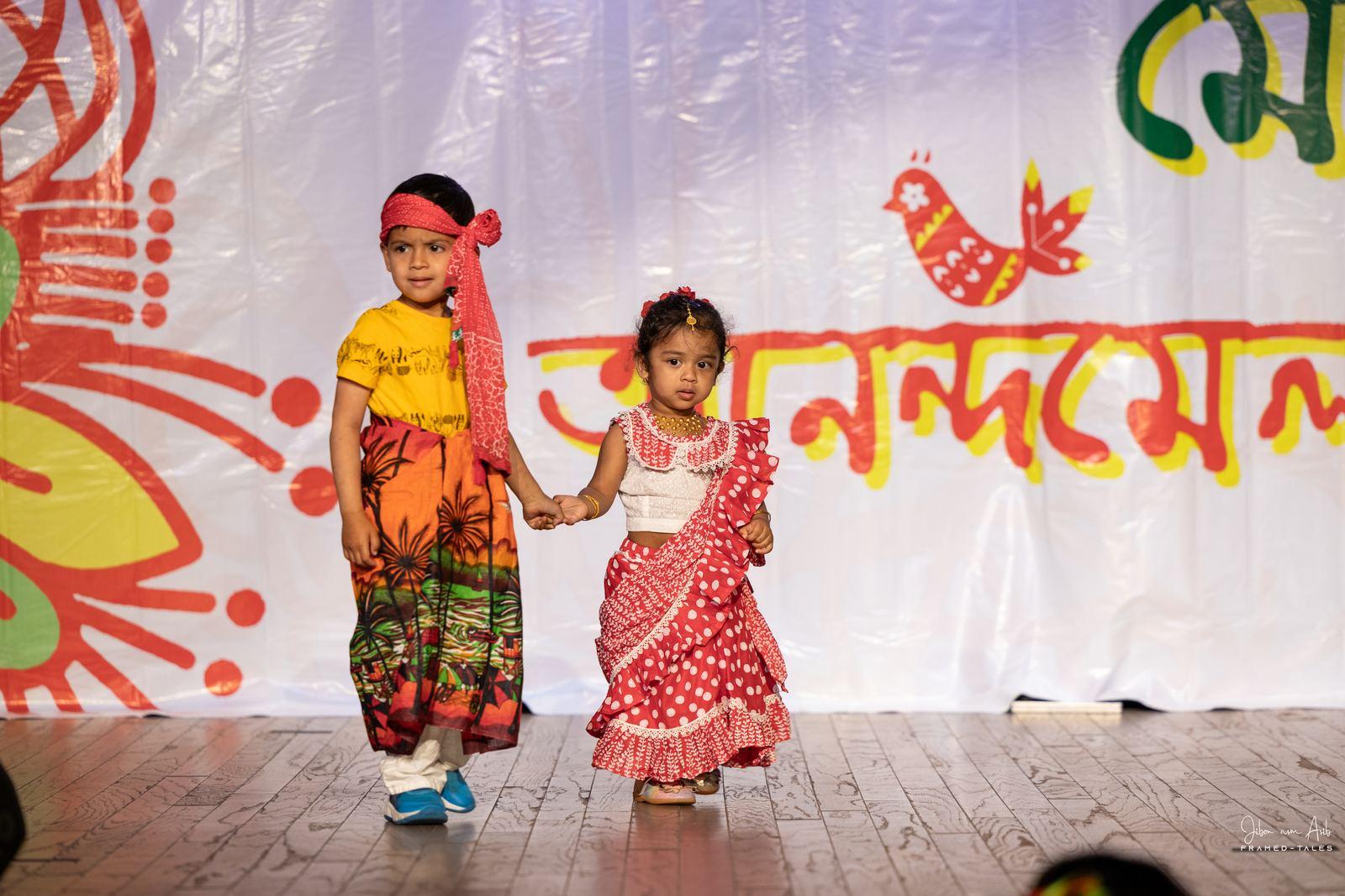 Boy in lungi and headband holding hands with a girl in polka-dot saree