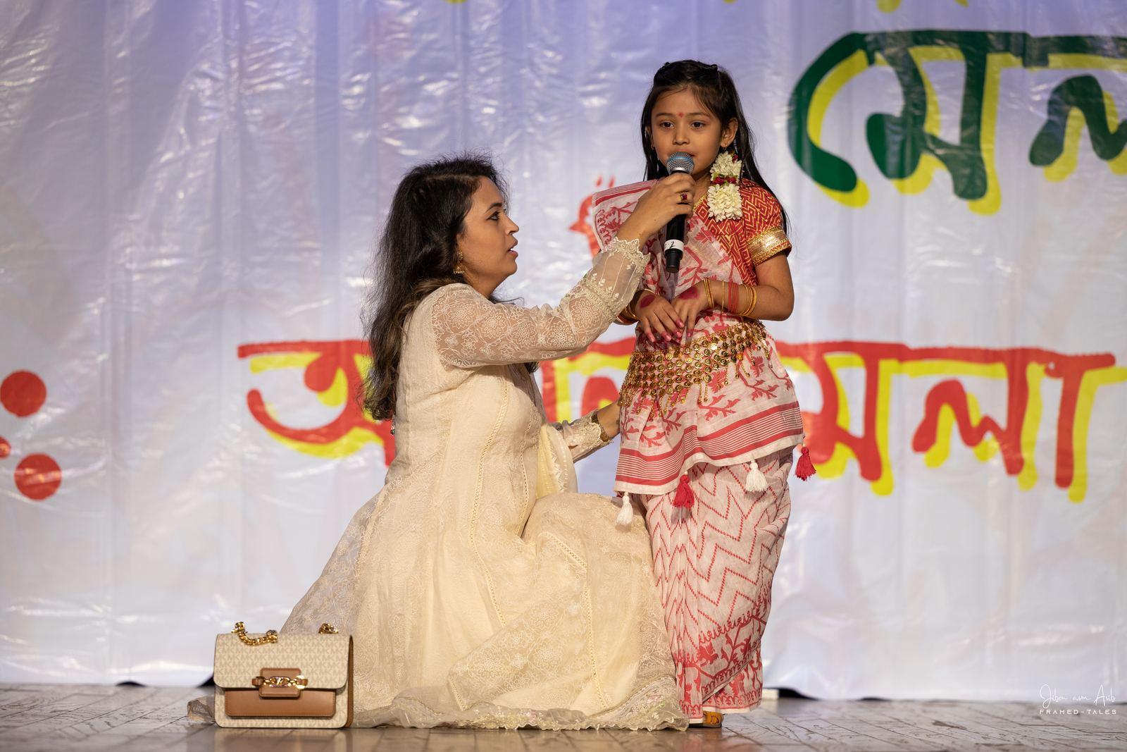Mother kneeling beside a girl in costume holding a mic